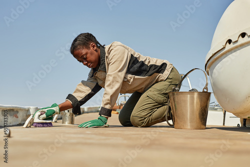 Side view portrait of black young woman cleaning and repairing floors on boat in sunlight, copy space