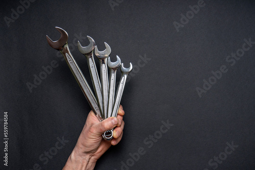 Men's hand holding set of wrenches on black background. Tools in human hand. Man worker with spanners. Technique repair, equipment for mechanical service, labor or father's day concept