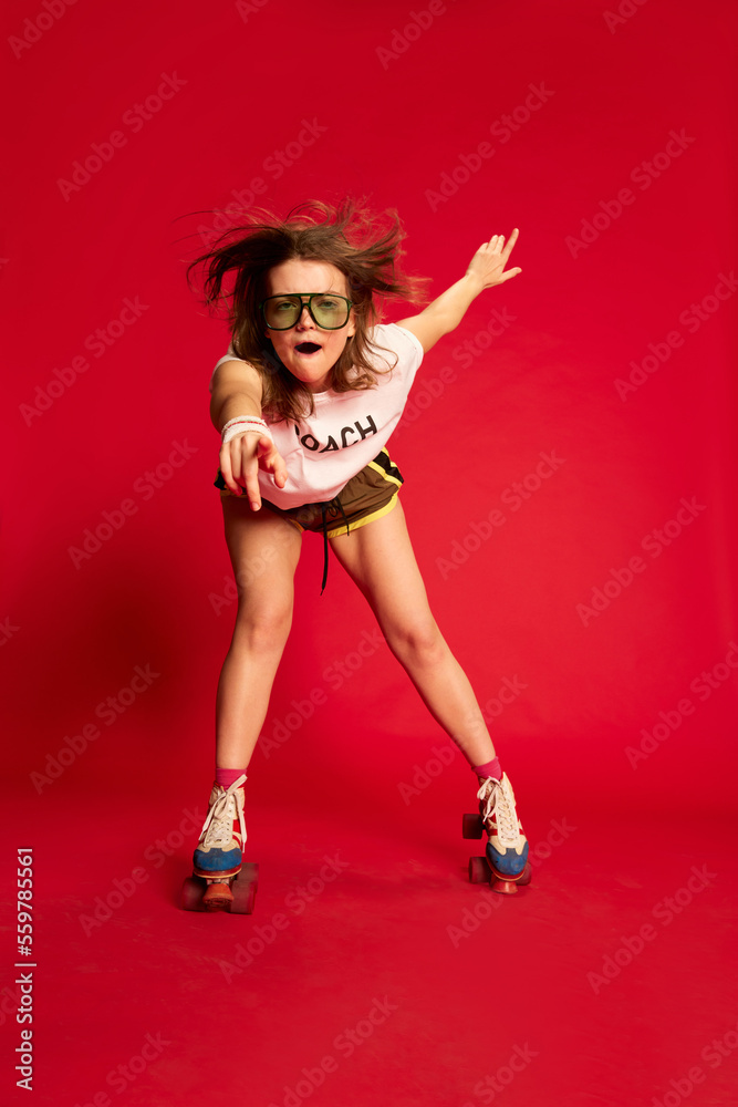 Delight. Portrait of fashionable stylish young girl in t-shirt and shorts rollerblading over red background. Youth, fashion, happy emotions and active lifestyle concept Delight. Portrait of fashionable stylish young girl in t-shirt and shorts rollerblading over red background. Youth, fashion, happy emotions and active lifestyle concept