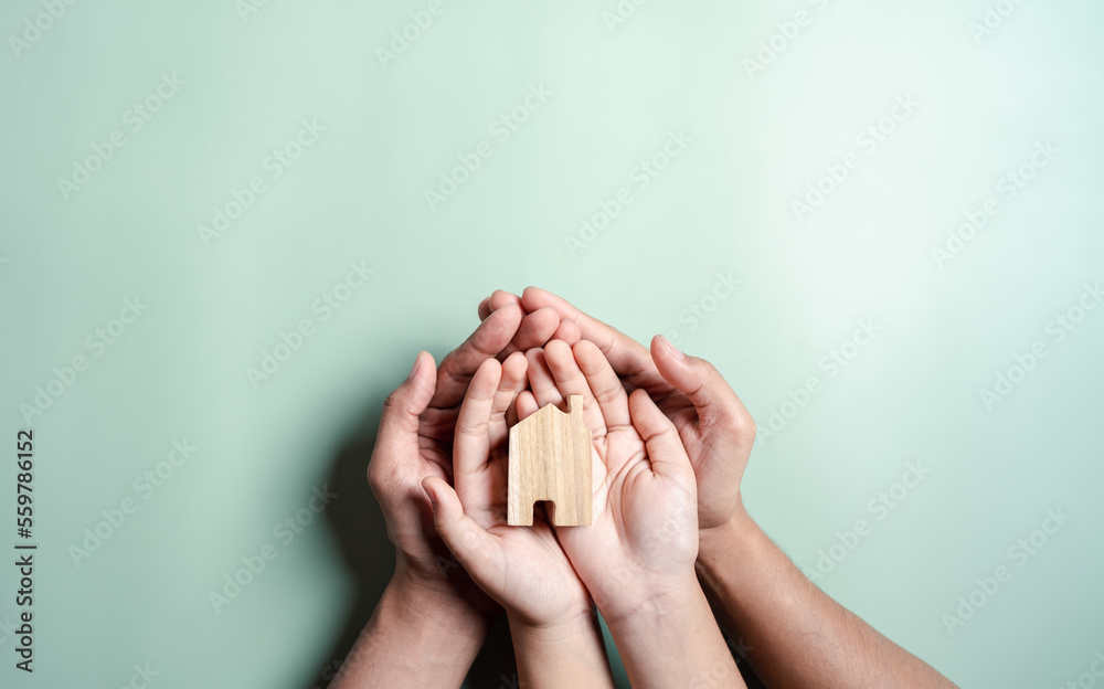 Hands holding wooden house, family home, homeless housing, mortgage crisis and home protecting insurance, international day of families, foster home care, family day care, stay home concept Hands holding wooden house, family home, homeless housing, mortgage crisis and home protecting insurance, international day of families, foster home care, family day care, stay home concept