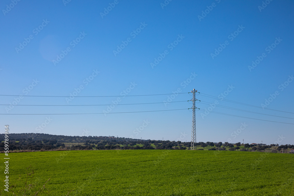 view of the countryside with green grass and mountains behind in blue sky day with electric tower crossing the landscape view of the countryside with green grass and mountains behind in blue sky day with electric tower crossing the landscape