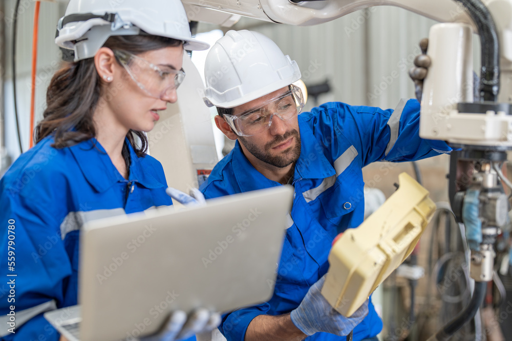 Male and female engineer training using remote controller control robot arm welding machine in industrial factory. Team of technician automation robot in uniform explains robot arm system. Male and female engineer training using remote controller control robot arm welding machine in industrial factory. Team of technician automation robot in uniform explains robot arm system.