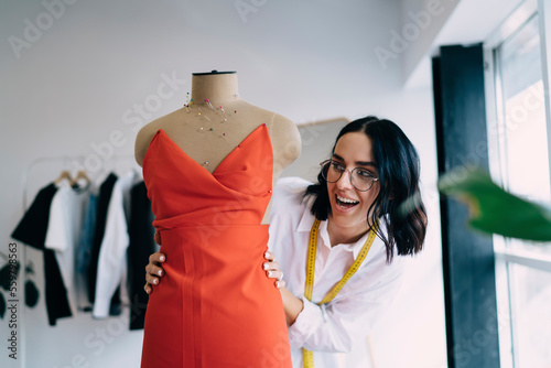 Canvas Print Joyful ethnic female dressmaker standing beside mannequin