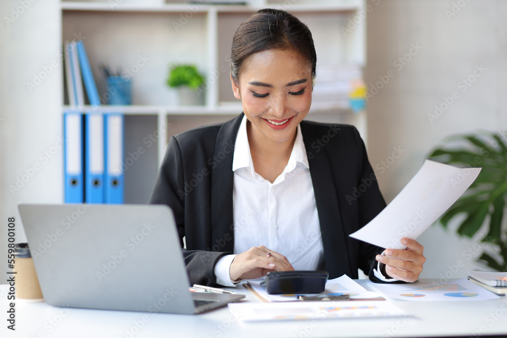 Businesswoman accountant in an accounting firm working with financial audits and budgeting using a calculator and laptop. Businesswoman accountant in an accounting firm working with financial audits and budgeting using a calculator and laptop.