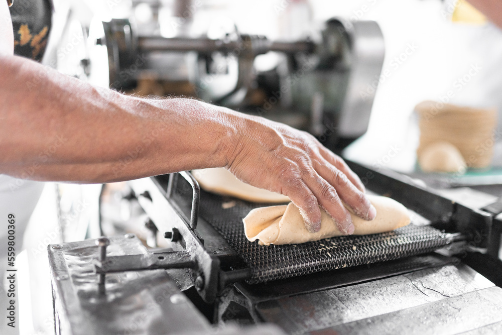 An adult tortilla maker is grabbing some corn tortillas from the hot conveyor belt. Close up