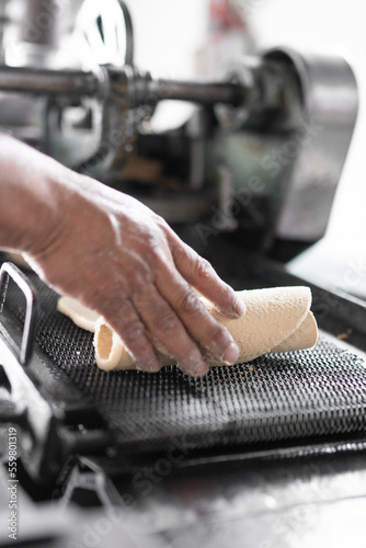 An adult tortilla maker is grabbing some corn tortillas from the hot conveyor belt. Close up © Miguel Serrano