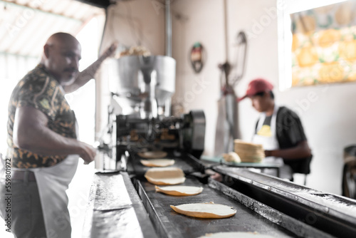 An adult man is working with his son producing corn tortillas with a nixtamall mill