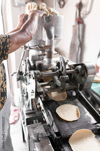 An adult tortilla maker is dropping some corn dough into the nixtamall mill in Mexico. Close up