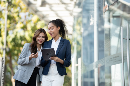 Two Asian businesswomen discussing business information while standing outside the office.