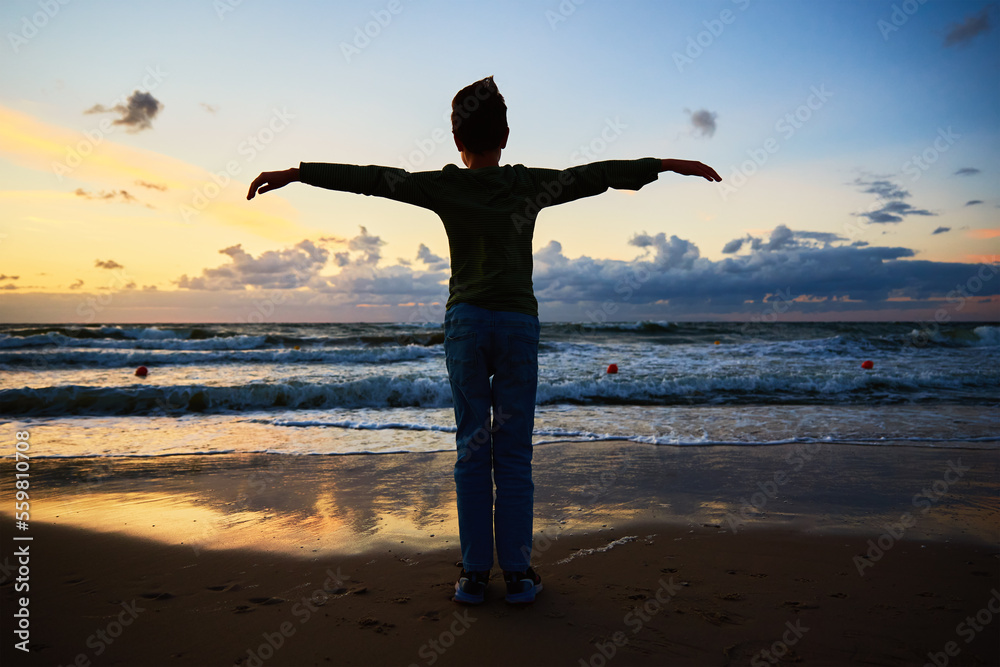 Boy silhouette standing on beach near sea and looking on the waves in sunset Boy silhouette standing on beach near sea and looking on the waves in sunset