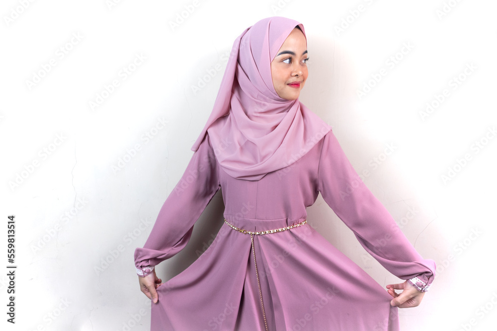 Beautiful smiling Asian woman in pink hijab raise the skirt and looking confident isolated over grey background Beautiful smiling Asian woman in pink hijab raise the skirt and looking confident isolated over grey background