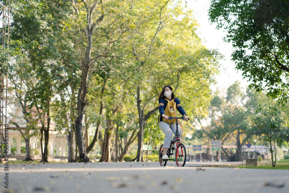 Obraz premium asian woman wearing facemask and biking bicycle with her cat in backpack at park