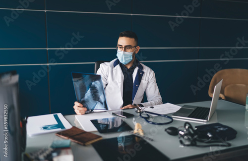 Concentrated male practitioner in mask working on chest x ray image