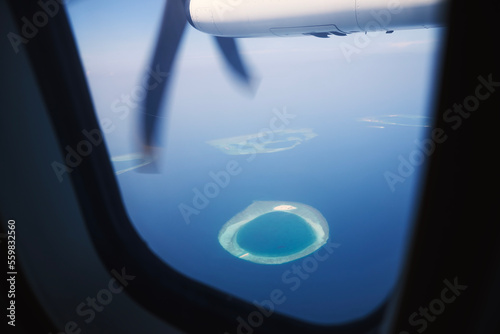View from turboprop airplane window in Maldives. Indian Ocean with beautiful tropical islands at idyllic sunny day..