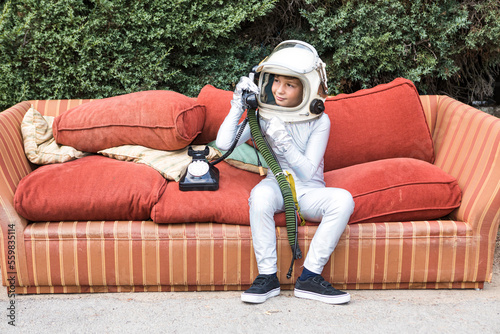 Boy in spacesuit having phone conversation on couch in park