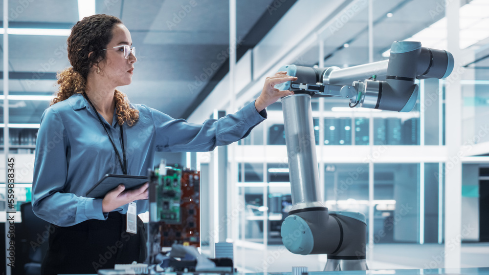 Portrait of a Young Multiethnic Female Engineer Using Tablet Computer. Interacting with a Robotic Arm Machine, Receiving a Microchip from the Hand. High Tech Industrial Laboratory Facility. Portrait of a Young Multiethnic Female Engineer Using Tablet Computer. Interacting with a Robotic Arm Machine, Receiving a Microchip from the Hand. High Tech Industrial Laboratory Facility.