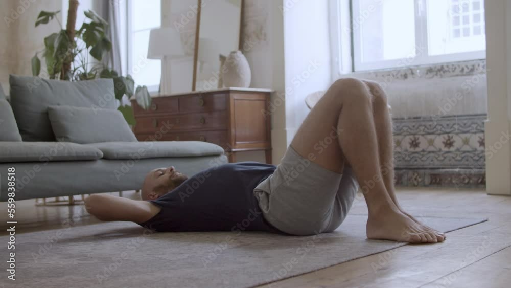 Focused Caucasian man exercising abs on floor at home. Cheerful bearded athlete doing abdominal crunches in morning, working out, taking care of health on weekend. Sport, indoor activity concept Focused Caucasian man exercising abs on floor at home. Cheerful bearded athlete doing abdominal crunches in morning, working out, taking care of health on weekend. Sport, indoor activity concept