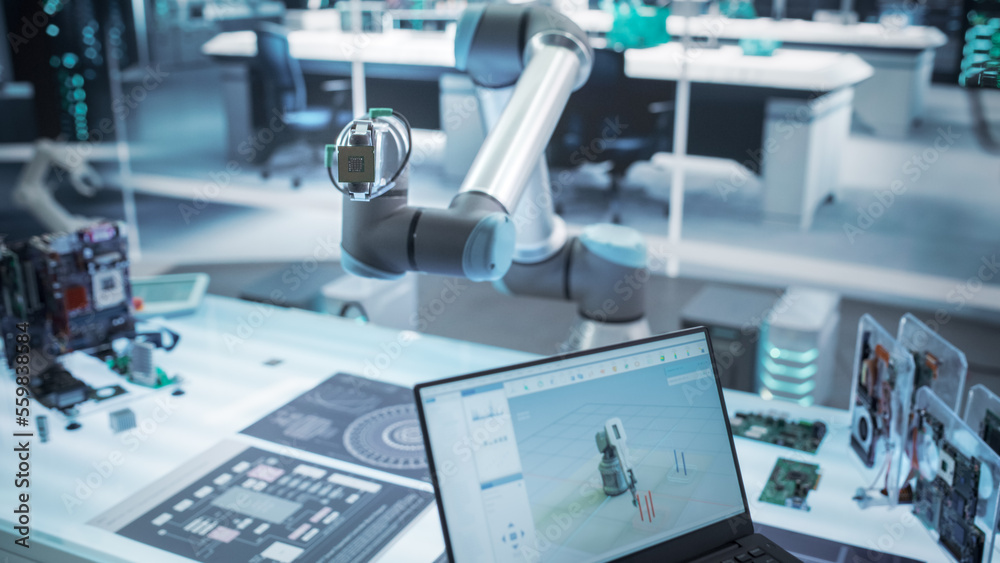 Fototapeta premium Over the Shoulder Shot of a Robotics Engineer Using a Laptop Computer with a Software Operating the Robotic Arm. Robot Hand Holding a Microchip. Automation Startup Research and Development Office.