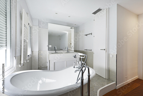 Bathroom with claw-foot bathtub  white wooden furniture with built-in mirror and white radiator towel rail and tiled tiles