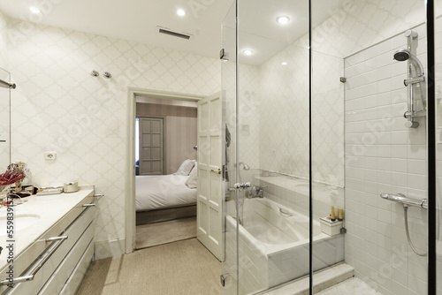 Bathroom with wall covered with white mosaic tile  two-bowl white marble sink with drawers and separate bathtub and shower cabin with glass door and partitions