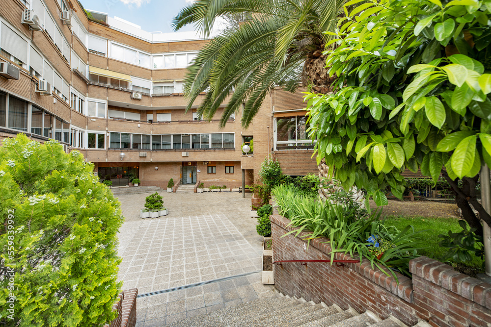 Facade of a four-story building with white aluminum windows and walkways with grass, slats and a recreation area with flowers and tree-lined gardens Facade of a four-story building with white aluminum windows and walkways with grass, slats and a recreation area with flowers and tree-lined gardens