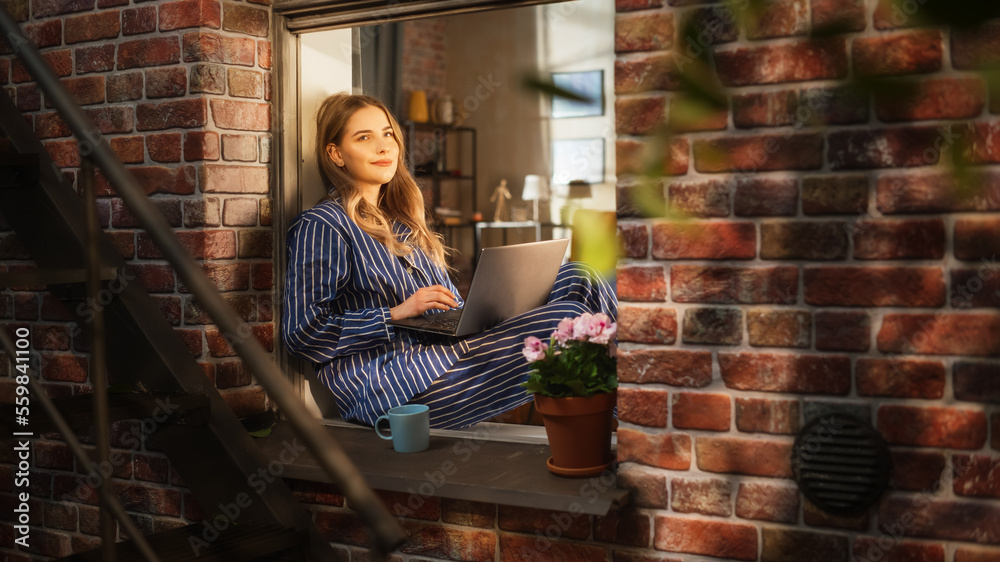 Female Manager Writing her Work Emails Using a Laptop While Sitting on her Windowsill. Young Beautiful Woman Enjoying Calmness and Comfort Thanks to the Possibility to do Remote Job