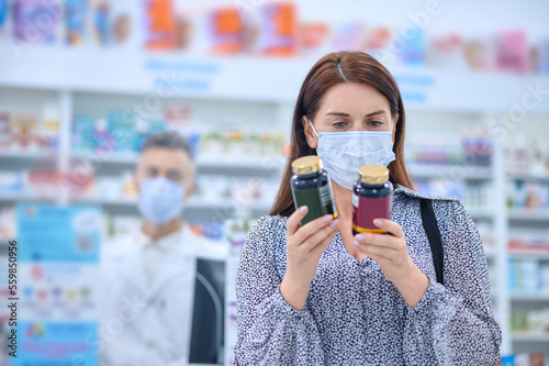 Woman in protective mask holding jars with vitamins in hands