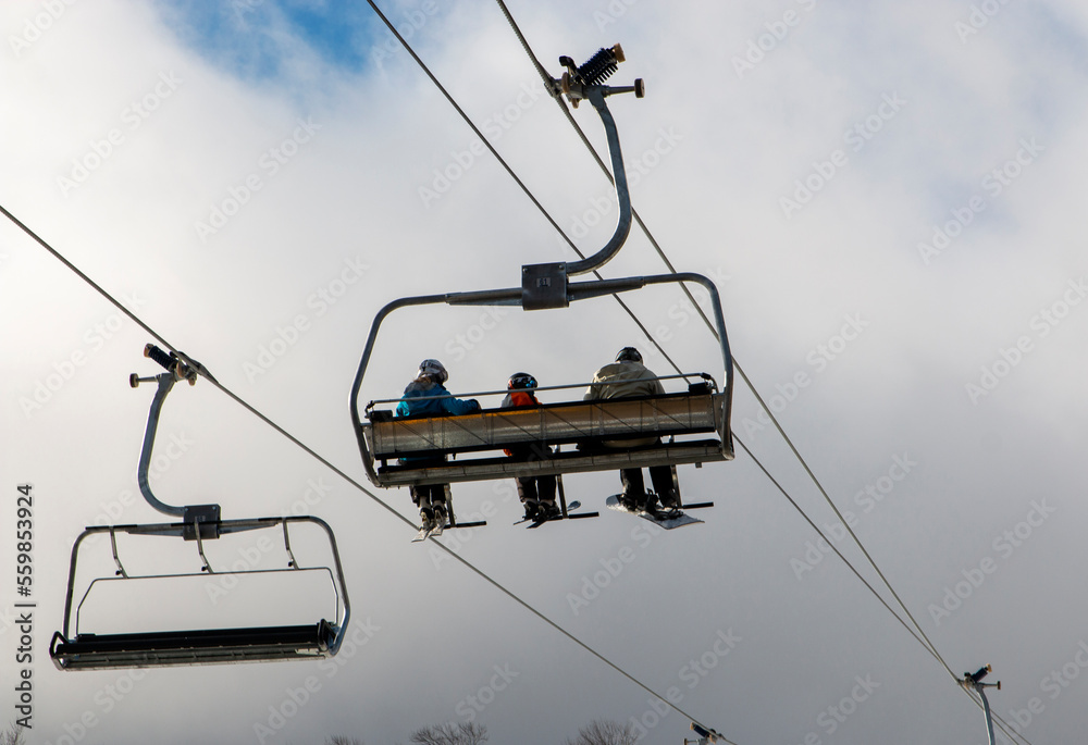 Three people riding a chair lift to the top of a mountain at Mount Snow