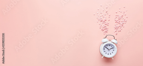 White alarm clock and pink hearts on pink background. Top view Background for Valentine's day.