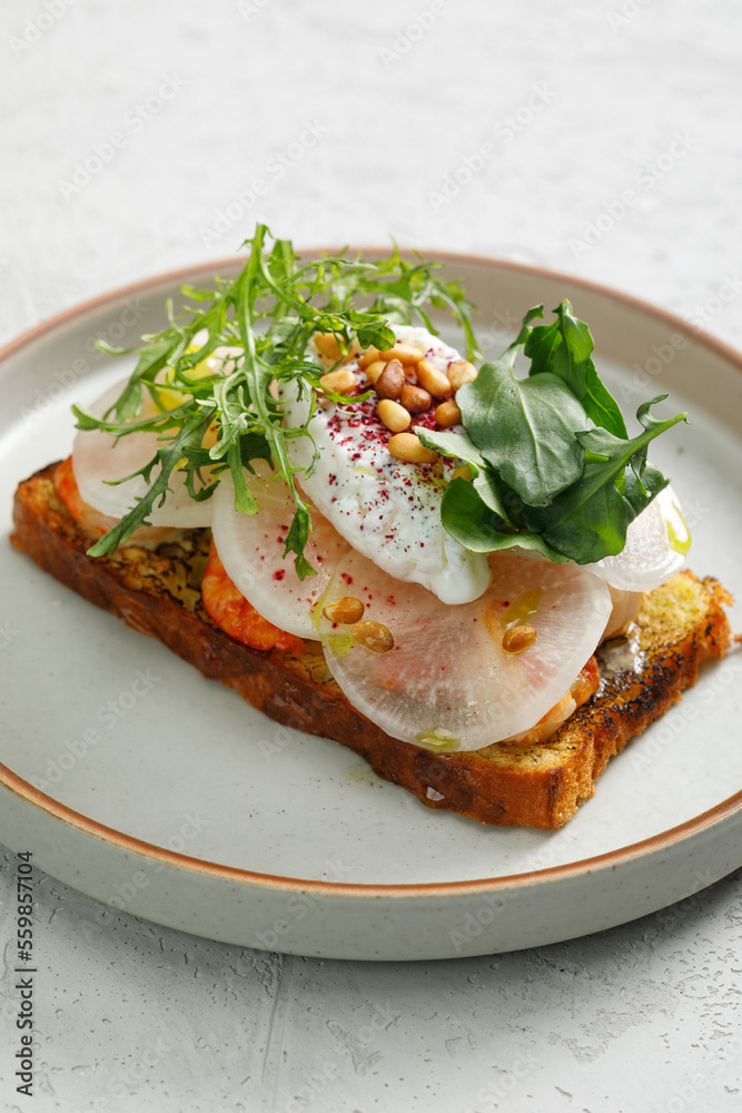 Toast with grilled shrimps and vegetables, poached egg and herbs on top served in restaurant.