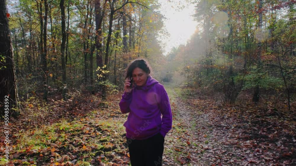 woman walking slowly through the autumn park in the evening and talking on the phone woman walking slowly through the autumn park in the evening and talking on the phone