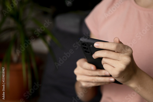 A close-up image of a teenage girl s hands using a smartphone at home in the living room  the concept of social networking  a set of SMS messages to her friends and classmates.