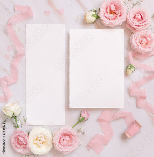 Blank paper cards between pink roses and pink silk ribbons on pink top view, wedding mockup © katrinshine
