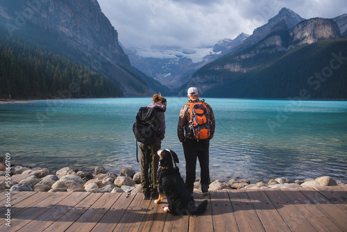 Young couple with backpacks and a dog. Tourists and travelers exploring Lake Louise in Banff, Canada.