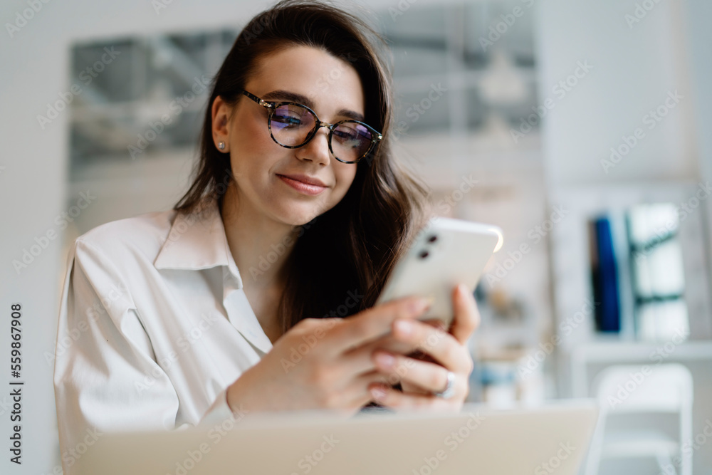 Content woman using smartphone while working on laptop Content woman using smartphone while working on laptop