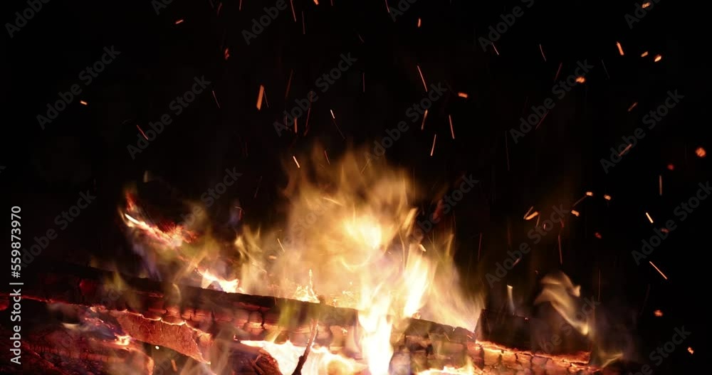 Burning log of wood and sparks close-up, slow motion. The hot embers of burning wood log fire. Firewood burning outdoors. Night fire bonfire embers. Smoldering fire