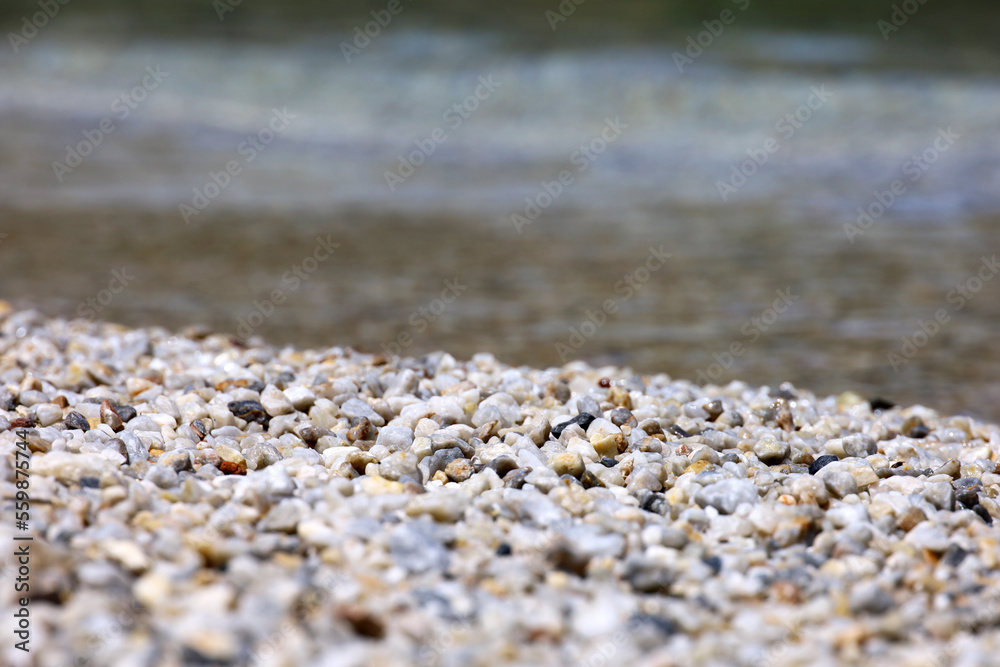 Small pebble stones on sea beach with transparent water. Natural background for summer vacation Small pebble stones on sea beach with transparent water. Natural background for summer vacation