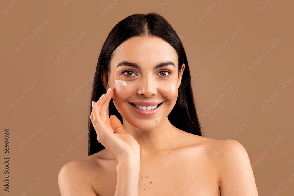 Cheerful sensual naked young woman using facial cream Cheerful sensual naked young woman using facial cream