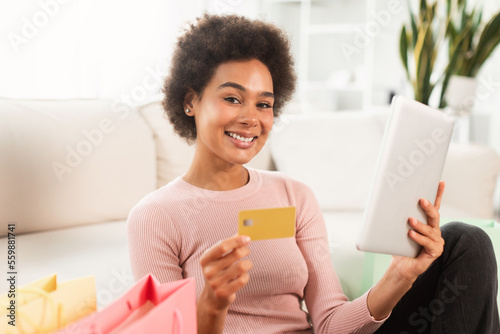 Glad happy young mixed race lady shopaholic with tablet and credit card checking financial bank account