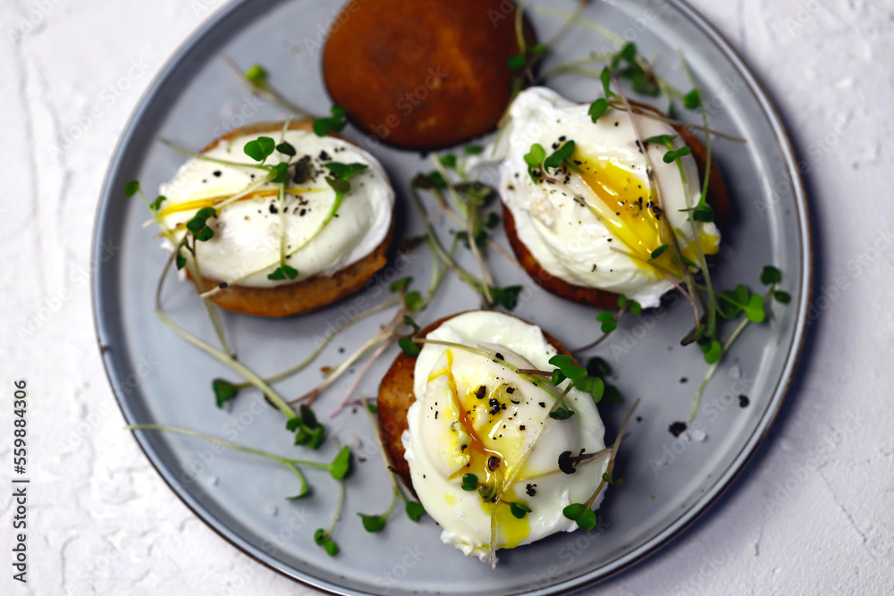 Poached eggs with microgreens on a crispy bun on a plate.