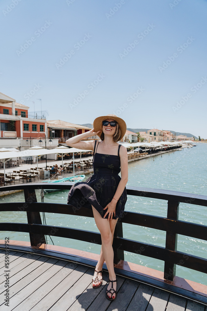 Happy woman traveler enjoying her vacation while standing in a dress on the bridge, playing with wind in Greece, Lefkada. Happiness, sea coast, sky