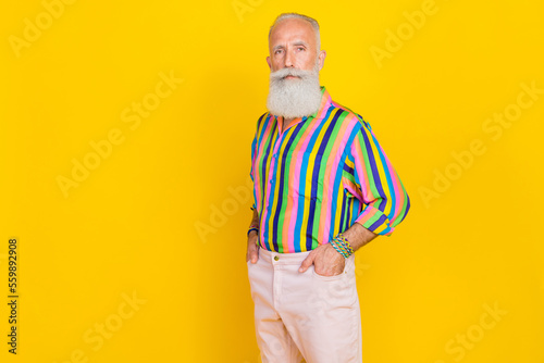 Photo of strict confident aged man put hands pockets empty space isolated on yellow color background photo