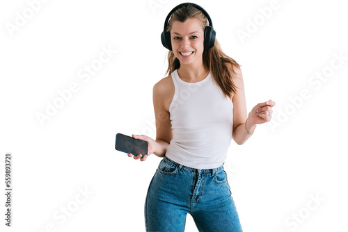 Cheerful hispanic young woman in casual using headphones and phone dancing against ransparent background looks at camera toothy smiles happy by new home. Beautiful female student having fun at home. photo