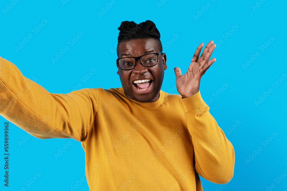Naklejka premium Cheerful Black Young Man Wearing Eyeglasses Taking Selfie Over Blue Background