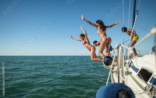 Multiracial friends jumping out of boat in the sea while having fun in their summer vacation - Luxury travel concept