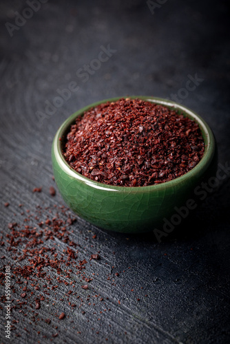 Dried ground red Sumac powder in a green bowl on dark background.