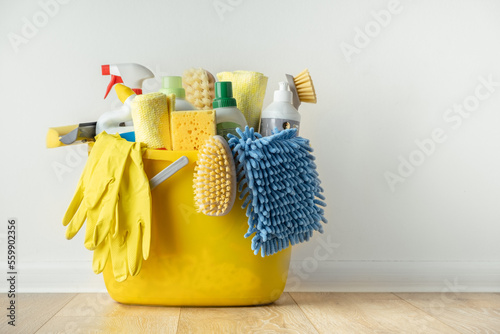 Brushes, bottles with cleaning liquids, sponges, rag and yellow rubber gloves on white background. Cleaning supplies in the yellow bucket on the wooden floor. Cleaning company service advertisement photo