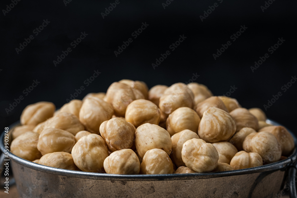 A pile of peeled hazelnuts in a metal bowl on the black background. Healthy nutrition concept. Traditional rustic agricultural background. Copy space for a free text. Macro shot A pile of peeled hazelnuts in a metal bowl on the black background. Healthy nutrition concept. Traditional rustic agricultural background. Copy space for a free text. Macro shot