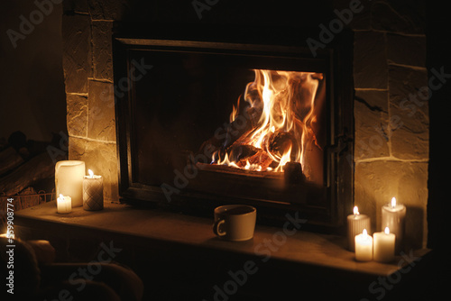 Fototapeta Warm cup of tea and candles at cozy burning fireplace in dark evening room
