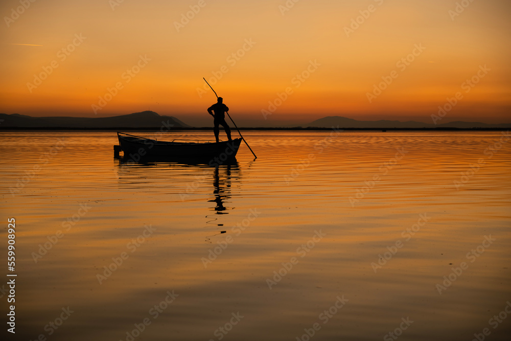 Sunset in Denizli Civril illuminated lake is approaching the shore with a fishing boat